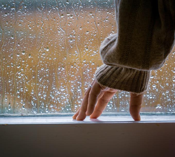 Henkilö seisoo sateisen ikkunan edessä. 