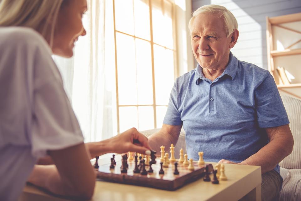 Ikääntynyt mies pelaa shakkia hoitajan tai tyttärensä kanssa