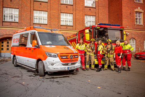 Ambulanssi, paloauto ja pelastushenkilöstöä paloaseman pihalla.