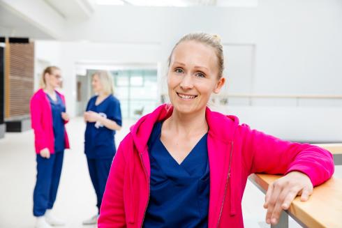 En sjuksköterska i en sjukhuskorridor tittar på kameran.