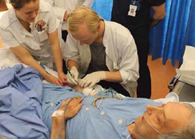 Opiskelijaryhmä tutkimassa sairaalasängyssä makaavaa potilasta.