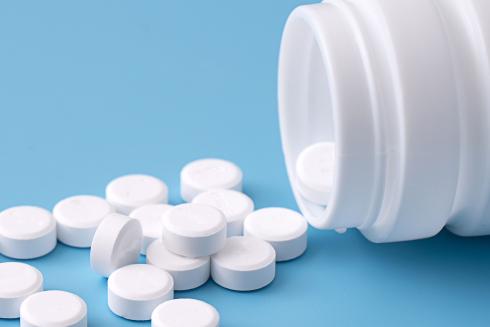 Valkoisia pyöreitä lääketabletteja sinisellä pinnalla. Tablettien vierellä kumolla valkoinen lääkepurkki.