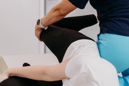 Fysioterapeutti taivuttaa potilaan jalkaa koukkuun. Potilas makaa kyljellään hoitopöydällä.
