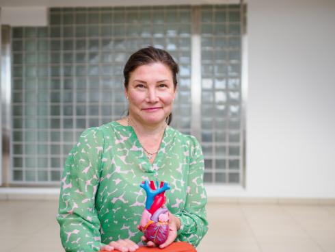 A person is standing in the lobby. They are wearing a shirt with a green and white pattern and in their hand is a model of a human heart. They smile for the camera.