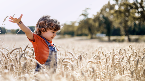 Hymyilevä lapsi levittelee käsiään sivuille lentokonetyyppisesti keskellä viljapeltoa.
