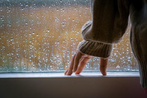 Henkilö seisoo sateisen ikkunan edessä. 