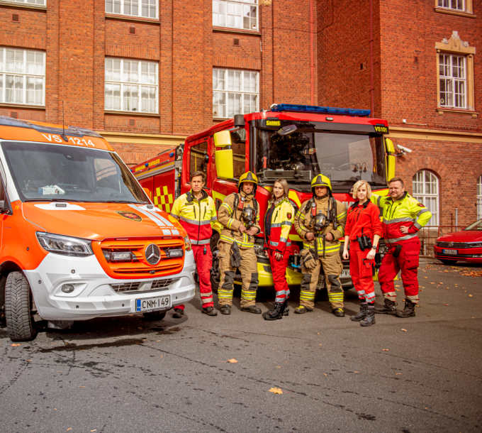 Ambulanssi, paloauto ja pelastushenkilöstöä paloaseman pihalla.