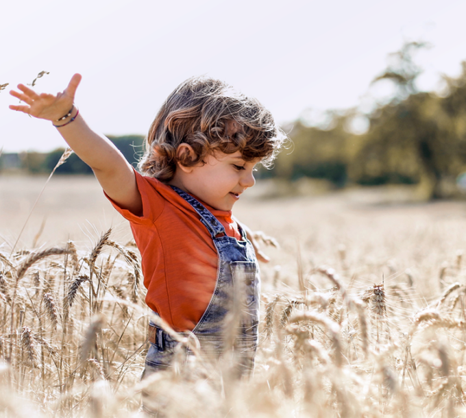 Hymyilevä lapsi levittelee käsiään sivuille lentokonetyyppisesti keskellä viljapeltoa.