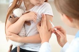 Lääkäri laittamassa rokotetta lapsen käsivarteen. Lapsella on sylissään pehmolelunalle.