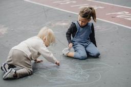 Kaksi lasta piirtävät liiduilla asfalttiin. 