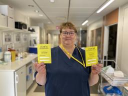 Tiina Hämäläinen, sairaanhoitaja sinisessä asussaan ja keltaiset elinluovutuskortit kädessään.