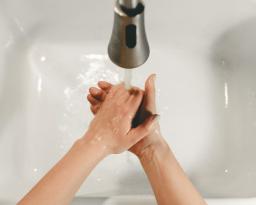 Henkilö pesee käsiänsä vesihanan alla.
