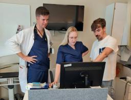 två läkare och en sjukskötare förbereder behandling och står vid en dator.